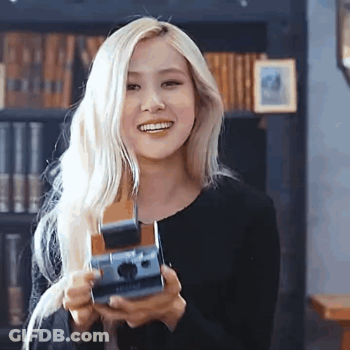 A Woman With Blonde Hair Is Holding A Camera In Her Hands And Smiling . GIF