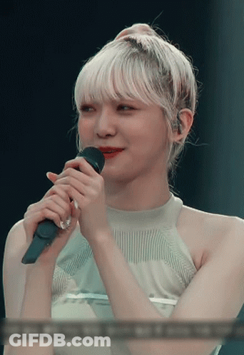 A Woman With Blonde Hair Is Holding A Microphone In Her Hand GIF