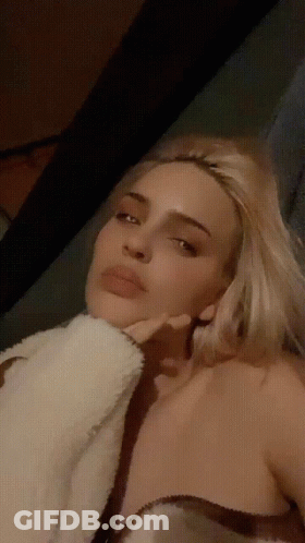 A Woman With Blonde Hair Is Laying Down With Her Hand On Her Chin GIF