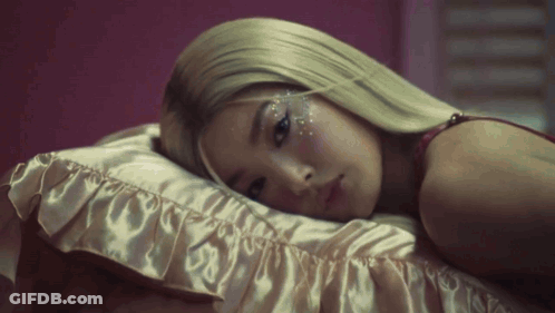 A Woman With Blonde Hair Is Laying On A Bed With A Pink Pillow . GIF