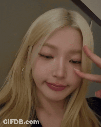 A Woman With Blonde Hair Is Making A Heart With Her Fingers GIF