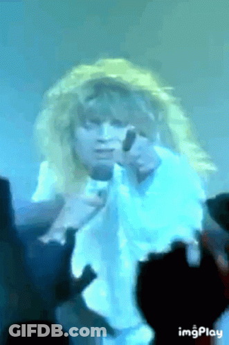 A Woman With Blonde Hair Is Singing Into A Microphone While A Crowd Watches . GIF