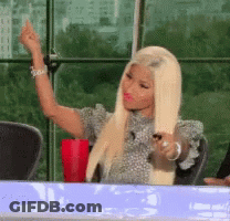 A Woman With Blonde Hair Is Sitting At A Table Giving A Middle Finger GIF