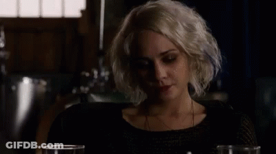 A Woman With Blonde Hair Is Sitting At A Table With Two Glasses Of Wine . GIF