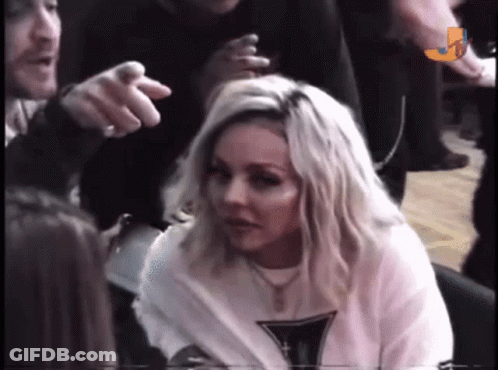 A Woman With Blonde Hair Is Sitting In A Crowd While A Man Points At Her . GIF