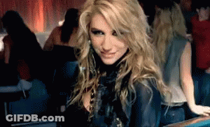 A Woman With Blonde Hair Is Sitting In A Dark Room Looking At The Camera GIF