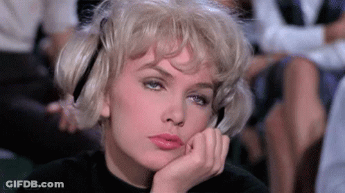 A Woman With Blonde Hair Is Sitting In A Theatre With Her Hand On Her Chin . GIF