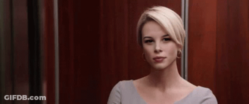 A Woman With Blonde Hair Is Sitting In An Elevator And Looking At The Camera . GIF