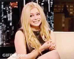 A Woman With Blonde Hair Is Sitting On A Couch Smiling . GIF
