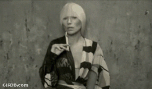 A Woman With Blonde Hair Is Smoking A Cigarette In A Black And White Photo . GIF