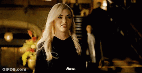 A Woman With Blonde Hair Is Standing In A Dark Room And Talking To A Man . GIF