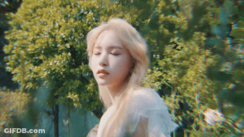 A Woman With Blonde Hair Is Standing In Front Of A Forest . GIF