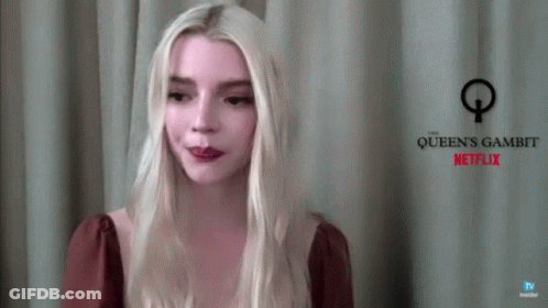 A Woman With Blonde Hair Is Standing In Front Of A Sign That Says Queen 'S Gambit Netflix GIF