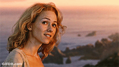 A Woman With Blonde Hair Is Standing In Front Of The Ocean GIF