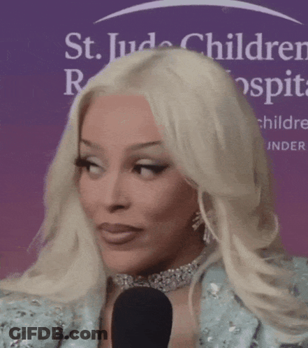 A Woman With Blonde Hair Is Talking Into A Microphone In Front Of A St. Jude Children 'S Hospital Sign GIF