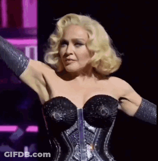 A Woman With Blonde Hair Is Wearing A Black Corset And Gloves On A Stage . GIF