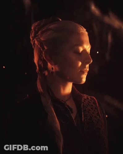 A Woman With Blonde Hair Is Wearing A Black Vest And A Necklace GIF