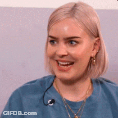 A Woman With Blonde Hair Is Wearing A Blue Shirt And Smiling . GIF