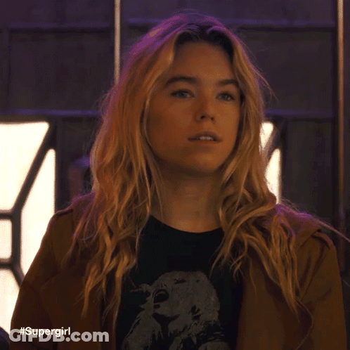 A Woman With Blonde Hair Is Wearing A Brown Jacket And A Black Shirt With A Picture Of An Eagle On It . GIF