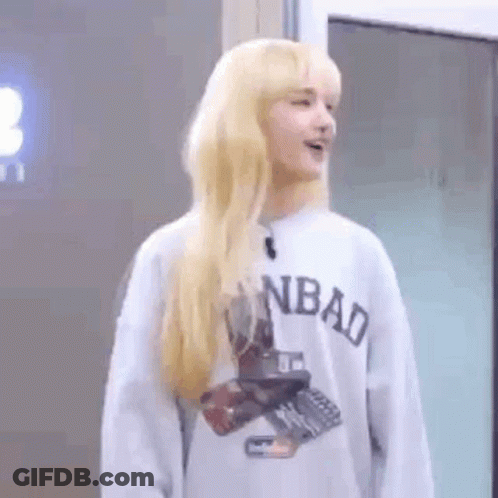 A Woman With Blonde Hair Is Wearing A Gray Sweatshirt And Standing In Front Of A Door . GIF