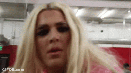 A Woman With Blonde Hair Is Wearing A Pink Shirt And Making A Funny Face GIF