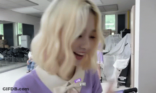 A Woman With Blonde Hair Is Wearing A Purple Sweater And A White Shirt . GIF