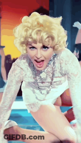 A Woman With Blonde Hair Is Wearing A White Dress And A Necklace GIF