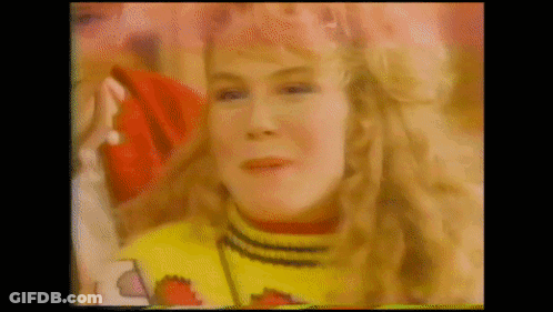 A Woman With Blonde Hair Is Wearing A Yellow Sweater And A Red Hat . GIF