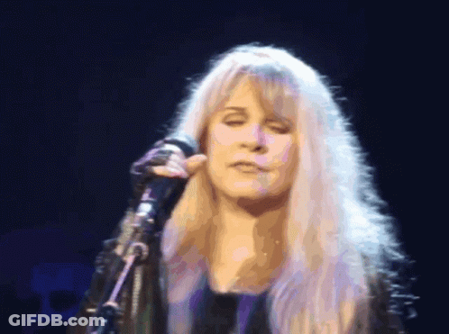 A Woman With Blonde Hair Singing Into A Microphone With Her Eyes Closed GIF