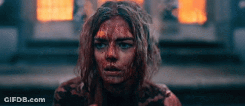 A Woman With Blood On Her Face Is Sitting In Front Of A Fire . GIF