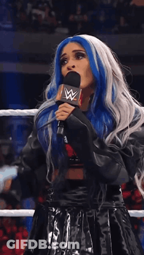 A Woman With Blue And White Hair Is Speaking Into A Microphone With A W Logo On It GIF