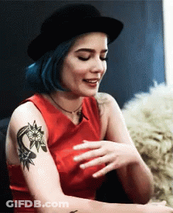 A Woman With Blue Hair And A Tattoo On Her Arm Is Wearing A Black Hat . GIF