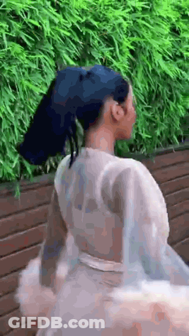 A Woman With Blue Hair And A White Dress Is Standing In Front Of A Wooden Fence . GIF