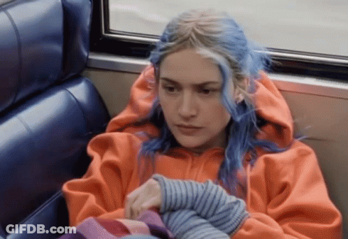 A Woman With Blue Hair And An Orange Hoodie Is Sitting On A Bus GIF