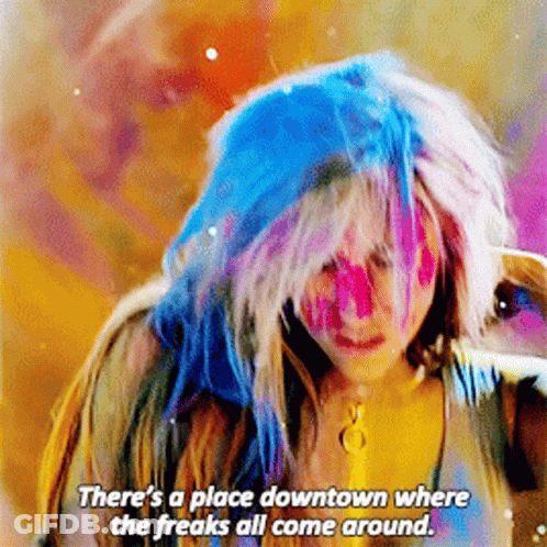 A Woman With Blue Hair And Pink Paint On Her Face Says " There 'S A Place Downtown Where The Freaks All Come Around " GIF