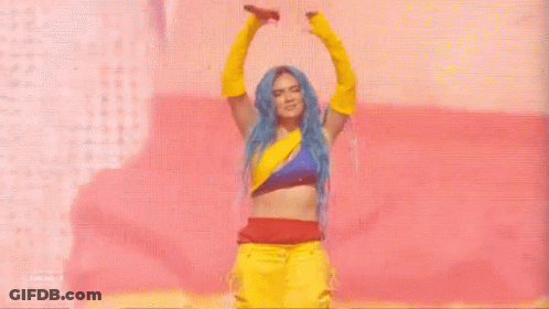 A Woman With Blue Hair And Yellow Gloves Is Dancing On A Stage With A Microphone . GIF