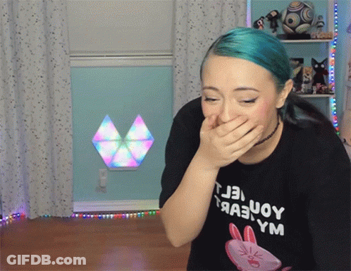 A Woman With Blue Hair Is Covering Her Mouth With Her Hand And Wearing A Black T-Shirt With A Rabbit On It GIF