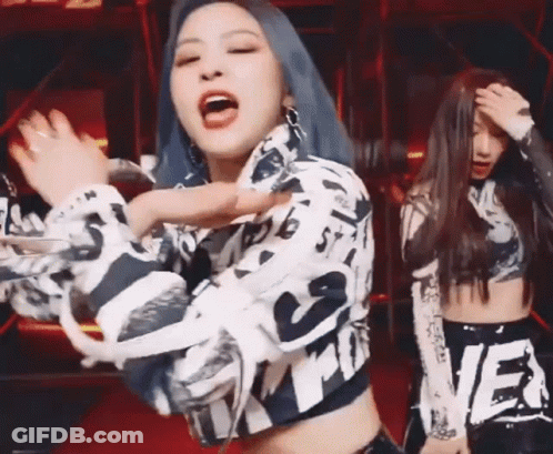 A Woman With Blue Hair Is Dancing With Another Woman In A Crop Top On A Stage . GIF
