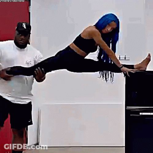 A Woman With Blue Hair Is Doing A Split On A Table While A Man Holds Her Legs . GIF