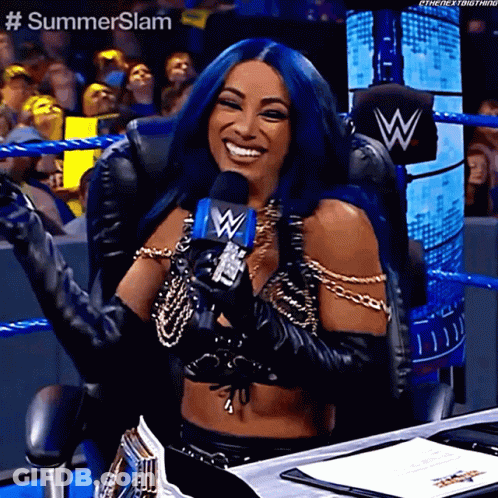 A Woman With Blue Hair Is Holding A Microphone And Smiling While Sitting In A Chair . GIF