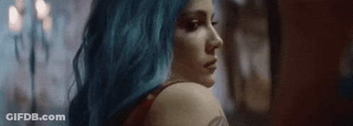 A Woman With Blue Hair Is Looking Over Her Shoulder At The Camera . GIF