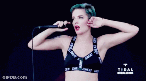 A Woman With Blue Hair Is Singing Into A Microphone While Wearing A Bra That Says Sweat Crew GIF