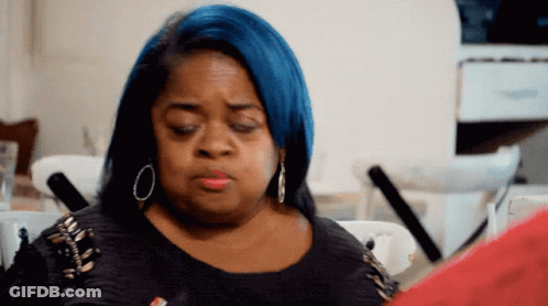 A Woman With Blue Hair Is Sitting At A Table Looking At A Piece Of Paper GIF
