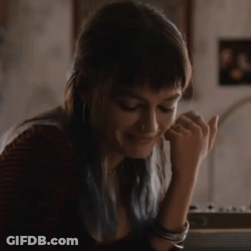 A Woman With Blue Hair Is Sitting At A Table With Her Hand On Her Chin . GIF