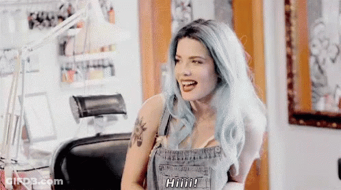 A Woman With Blue Hair Is Sitting In A Chair With Her Mouth Open And A Tattoo On Her Arm . GIF