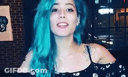A Woman With Blue Hair Is Standing In Front Of A Brick Wall And Smiling . GIF