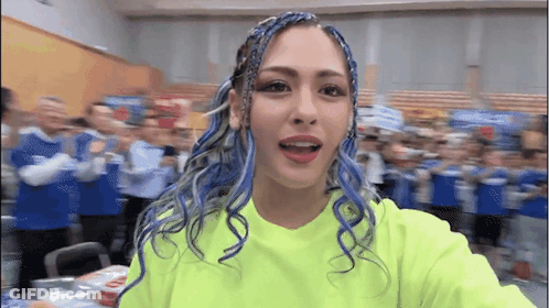 A Woman With Blue Hair Is Taking A Selfie In Front Of A Crowd . GIF