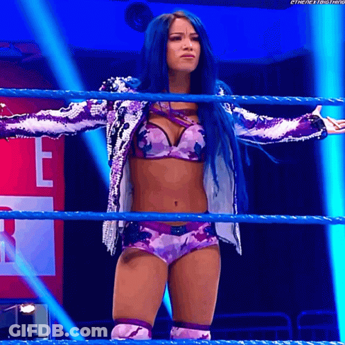 A Woman With Blue Hair Stands In A Wrestling Ring With Her Arms Outstretched GIF