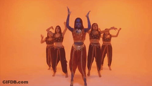 A Woman With Blue Paint On Her Face Is Kneeling In Front Of A Group Of Dancers GIF