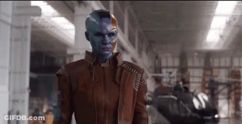 A Woman With Blue Paint On Her Face Is Wearing A Brown Jacket And Standing In A Warehouse . GIF